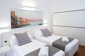 Een hotelkamer met twee bedden, een schilderij van een kustgezicht en een groot raam.