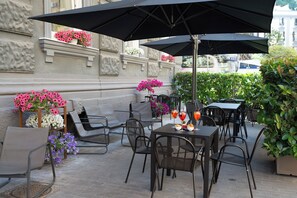 An outdoor seating area with tables and chairs, umbrellas, and flower arrangements. - Rex Lifestyle Hotel (Naples)