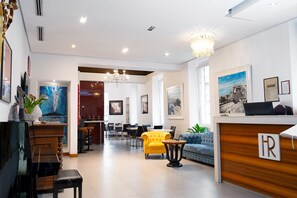 A hotel lobby with a reception desk, seating area, and artwork on the walls. - Rex Lifestyle Hotel (Naples)