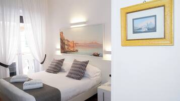 A hotel room with a bed, pillows, a bedside table, a nightstand, a framed picture, and a window with curtains.