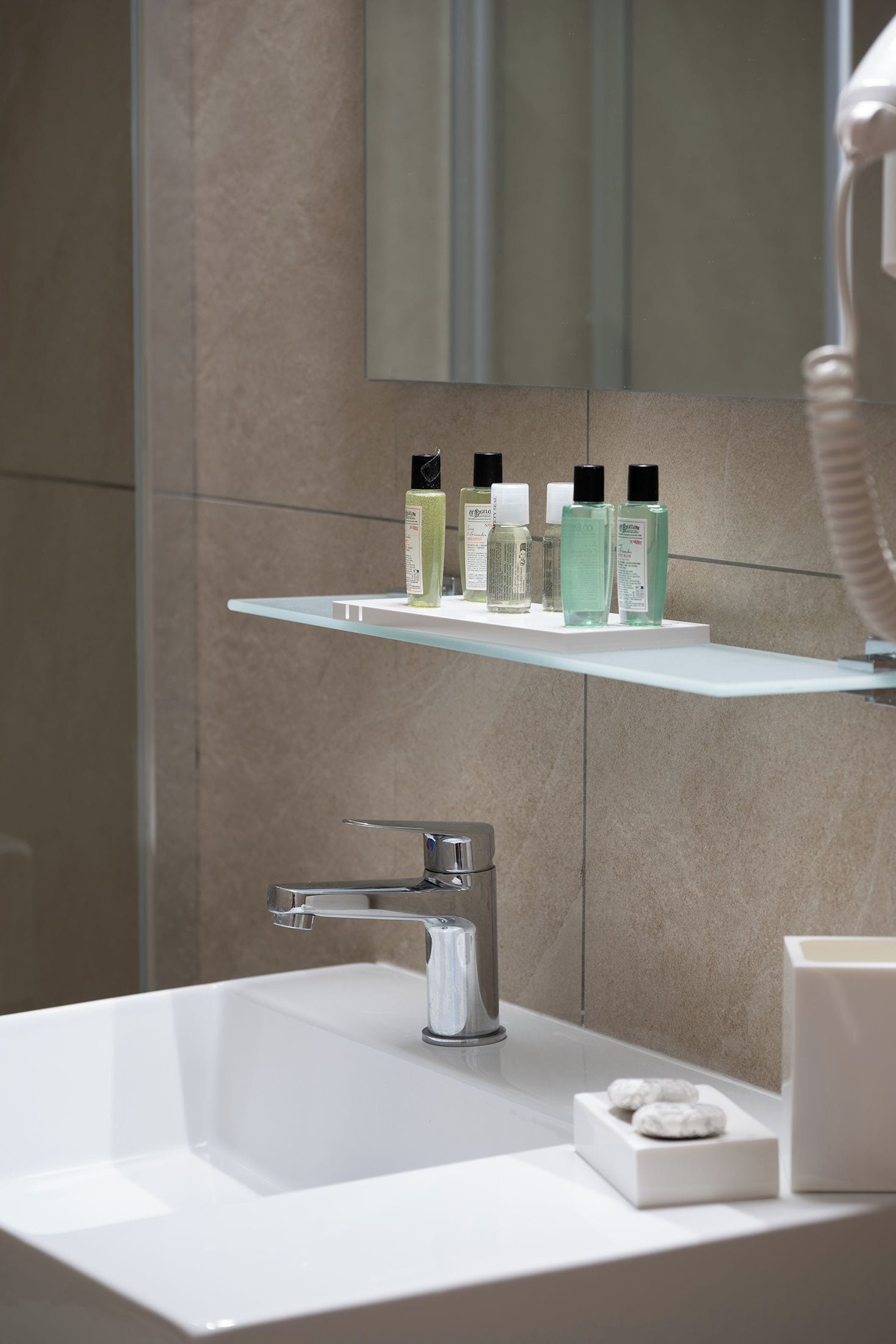 A bathroom with a white sink, chrome faucet, and a glass shelf holding toiletries.