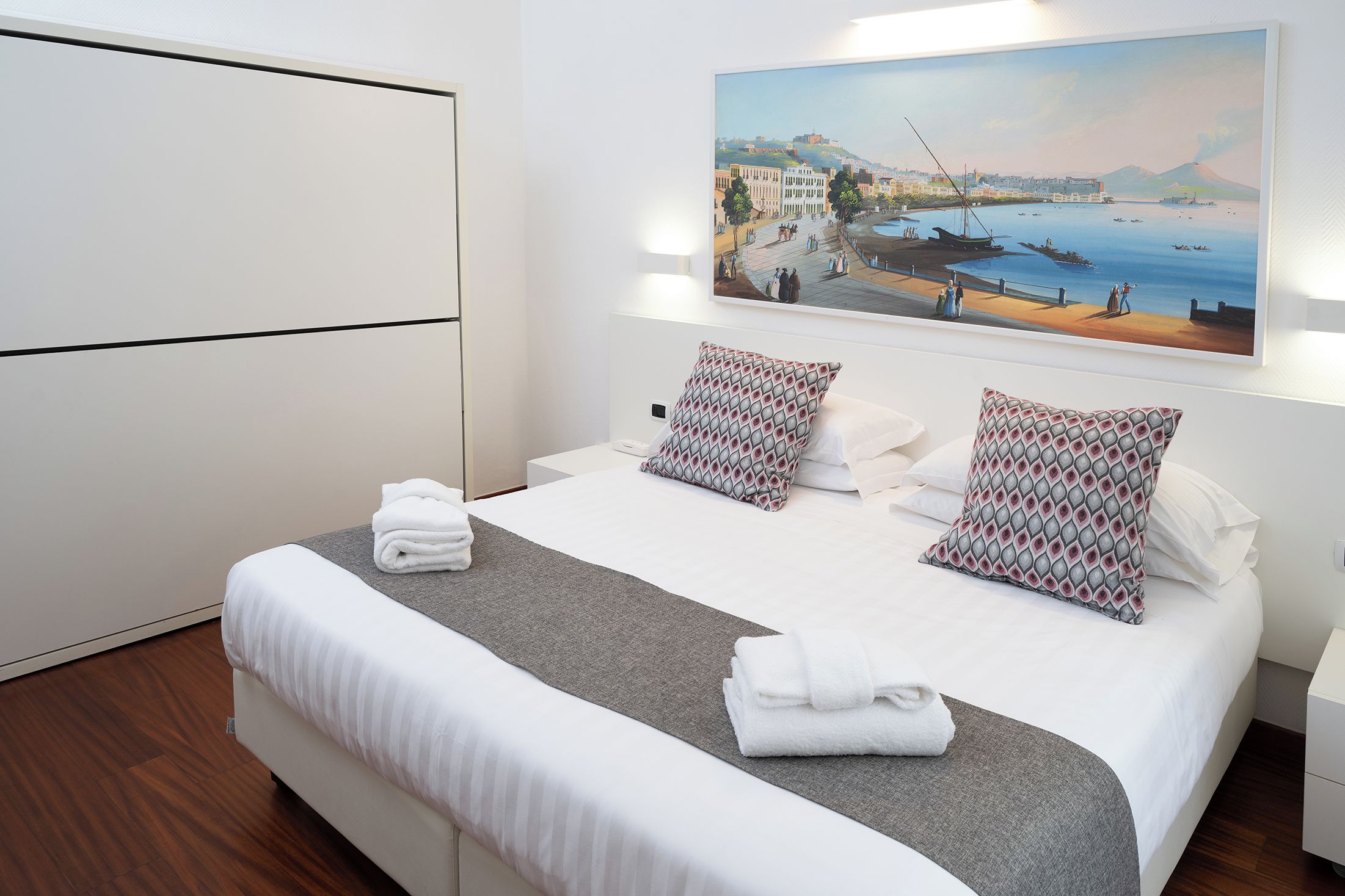 Une chambre d’hôtel avec un lit, des oreillers, un tableau et une armoire.