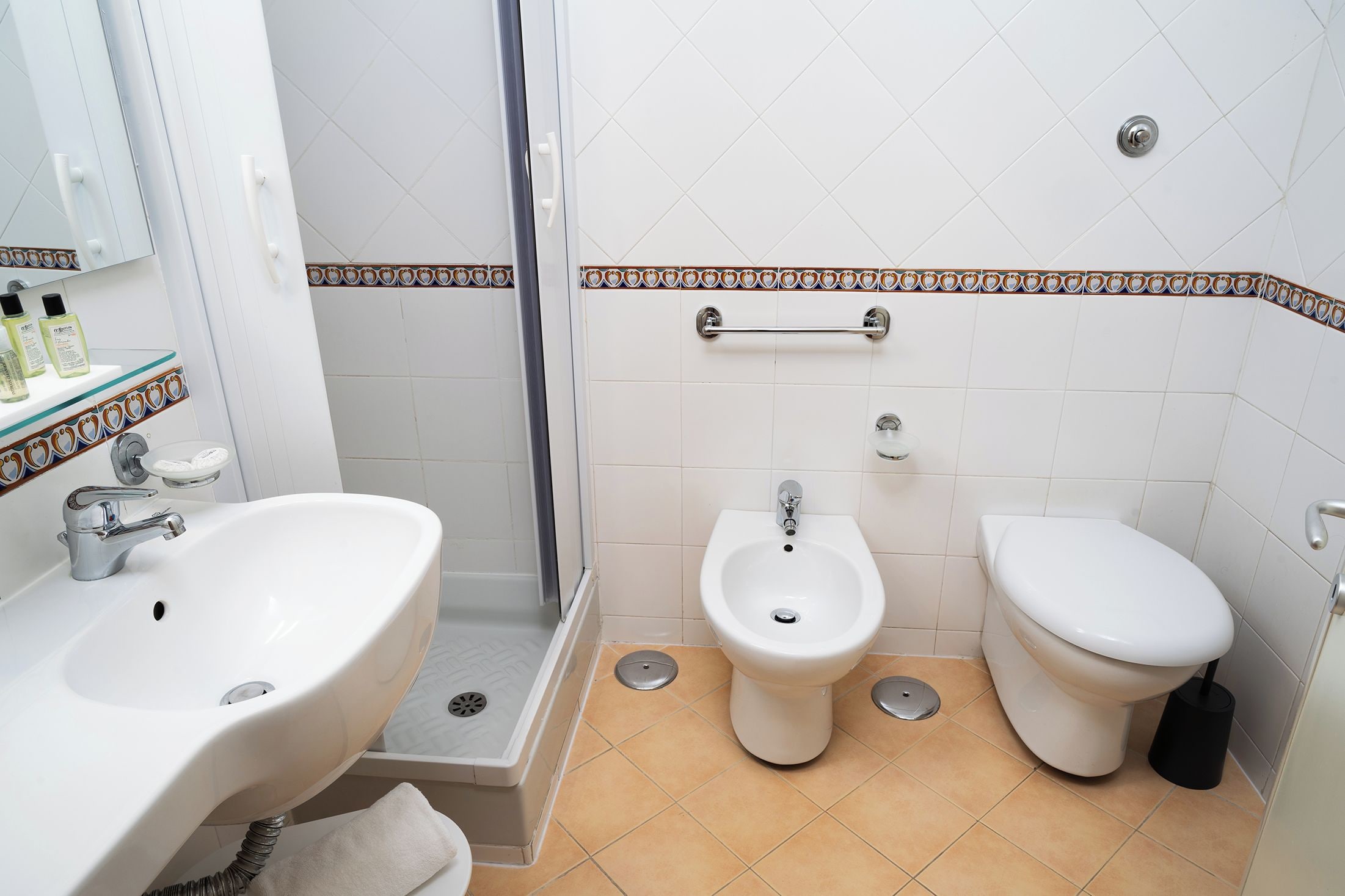 A bathroom with a sink, bidet, and toilet, a shower area, and a tiled floor.