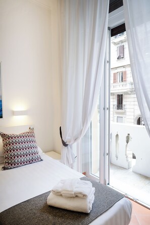 A hotel room with a bed, a view of the outside balcony, and a window with white curtains. - Rex Lifestyle Hotel (Naples)