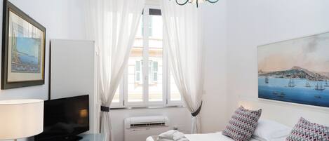Une chambre d’hôtel avec un lit, une télévision, un tableau et une fenêtre avec des rideaux.
