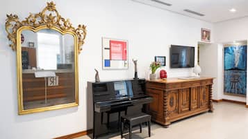 Une pièce agrémentée d’un grand miroir, d’un piano, d’une armoire en bois et d’œuvres d’art accrochées aux murs.