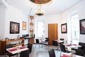 A modern dining area with a chandelier, framed artwork, and a buffet setup. - Rex Lifestyle Hotel (Naples)