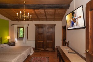 A bedroom with a bed, a wooden wardrobe, a dining table, and a television mounted on the wall.