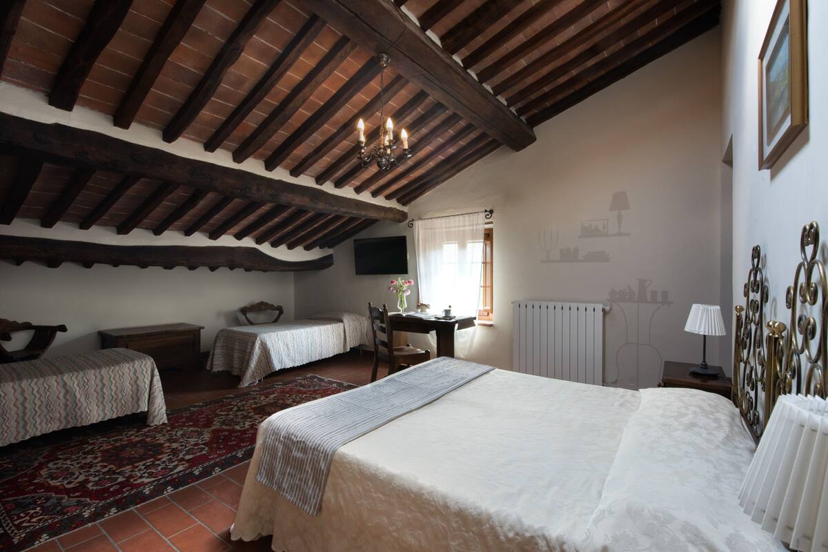 A bedroom with a large bed, two smaller beds, a wooden ceiling, a radiator, a desk, and a chair.