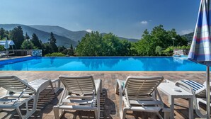 A swimming pool with lounge chairs and a table, surrounded by greenery and mountains. - Hotel Villa Rinascimento (Lucca)