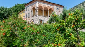 A stone building with a yellow facade and arched windows, surrounded by lush greenery and flowering plants. - Hotel Villa Rinascimento (Lucca)