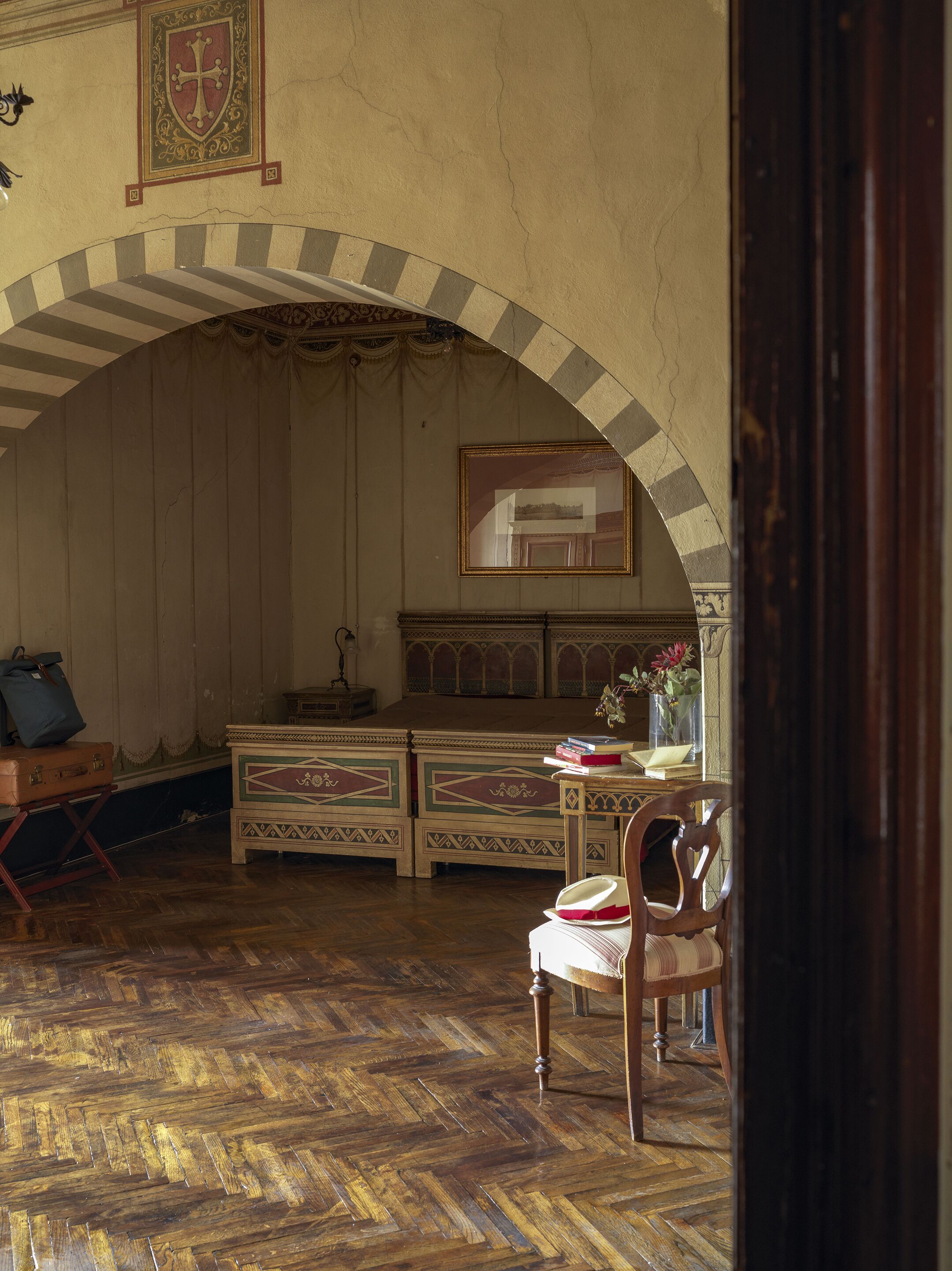 A room with a wooden herringbone floor, a wooden desk with a mirror, a chair, and a decorative arched ceiling.
