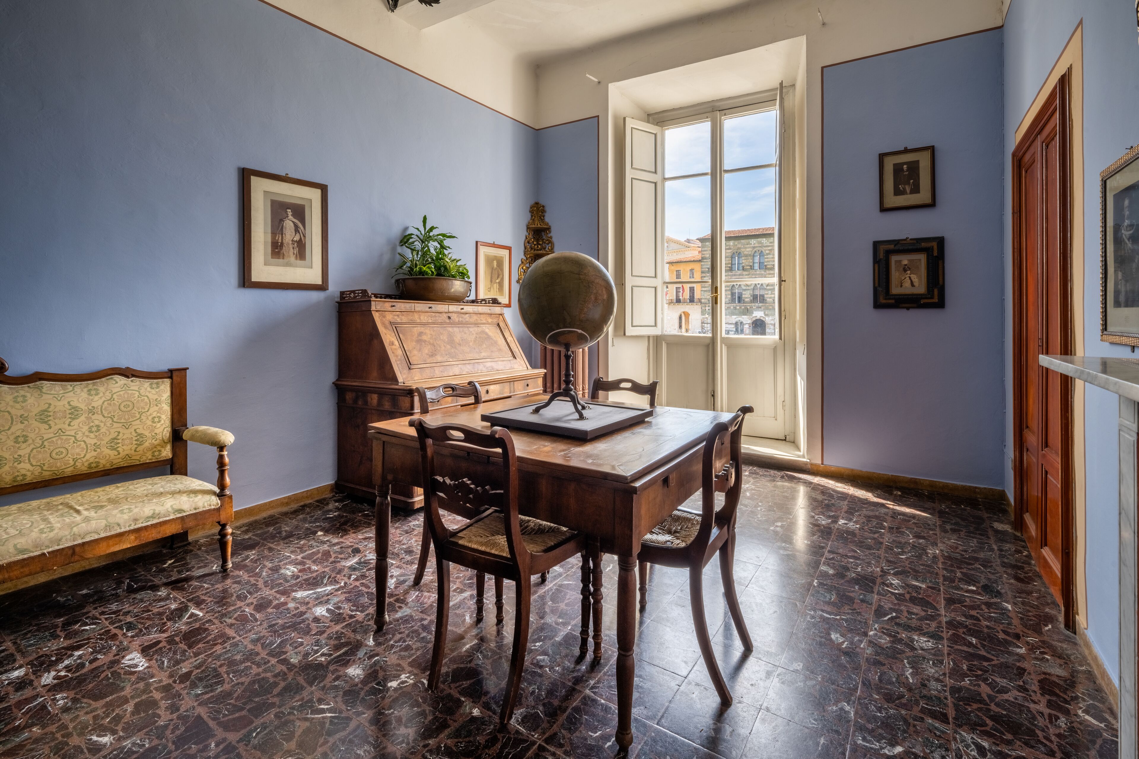 Une pièce avec une table en bois, des chaises, un canapé et une grande fenêtre donnant sur des immeubles.