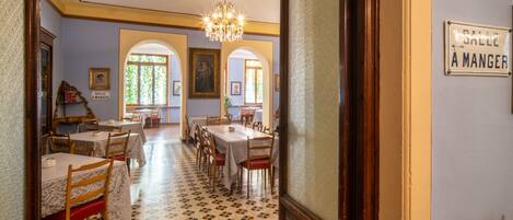 A dining area with tables and chairs, a chandelier, and a sign indicating the direction to the kitchen.