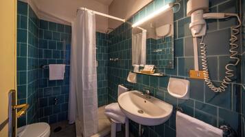 A bathroom with a shower, toilet, sink, and a hairdryer mounted on the wall.