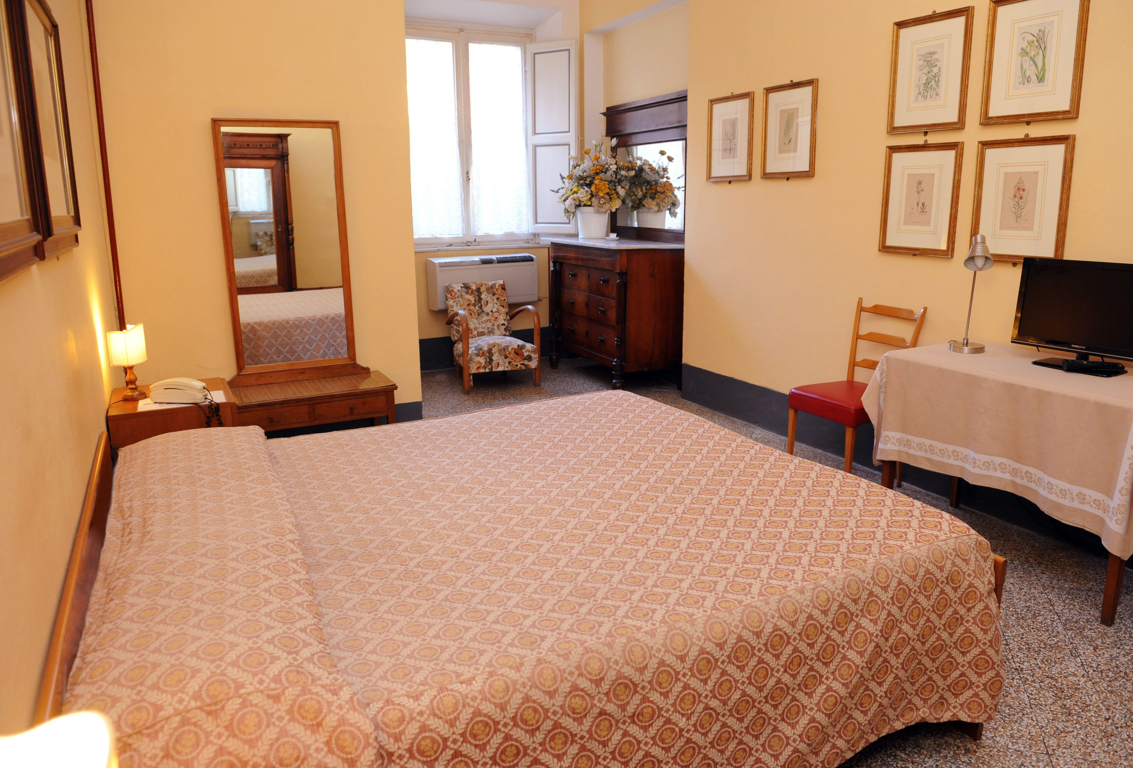 A hotel room with a large bed, a desk with a computer, a chair, a dresser, and a window with a view of another room.