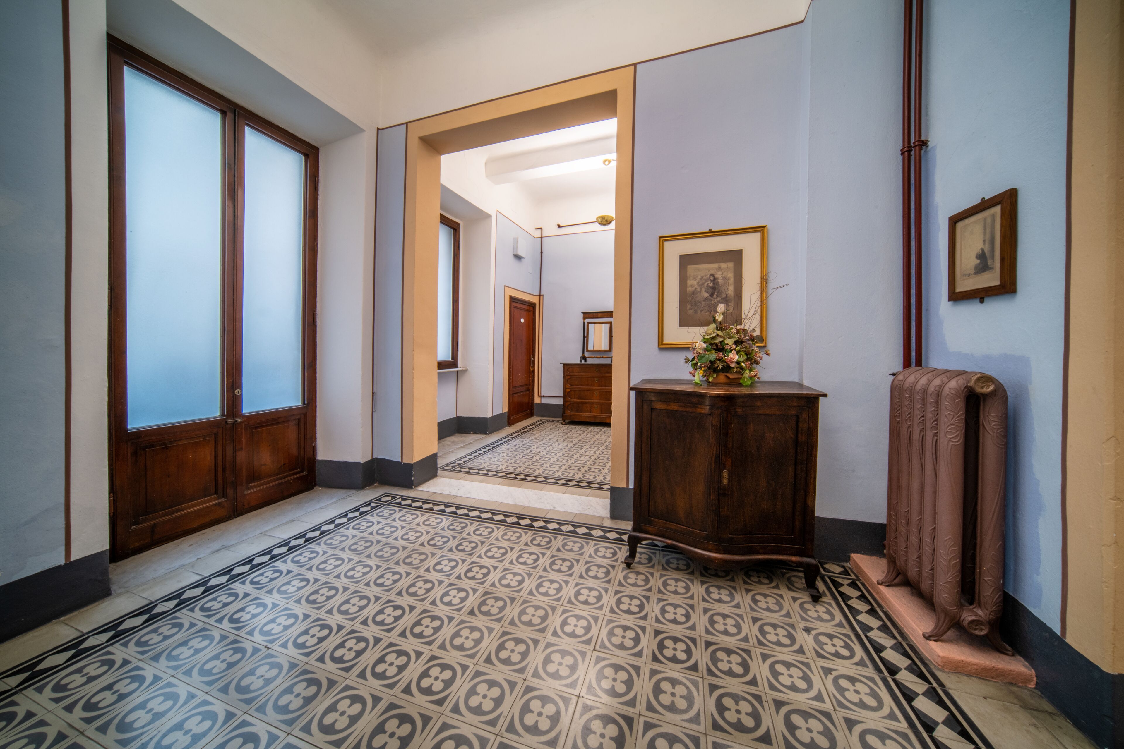 Un couloir avec des carreaux de sol à motifs, des portes en bois et un radiateur.