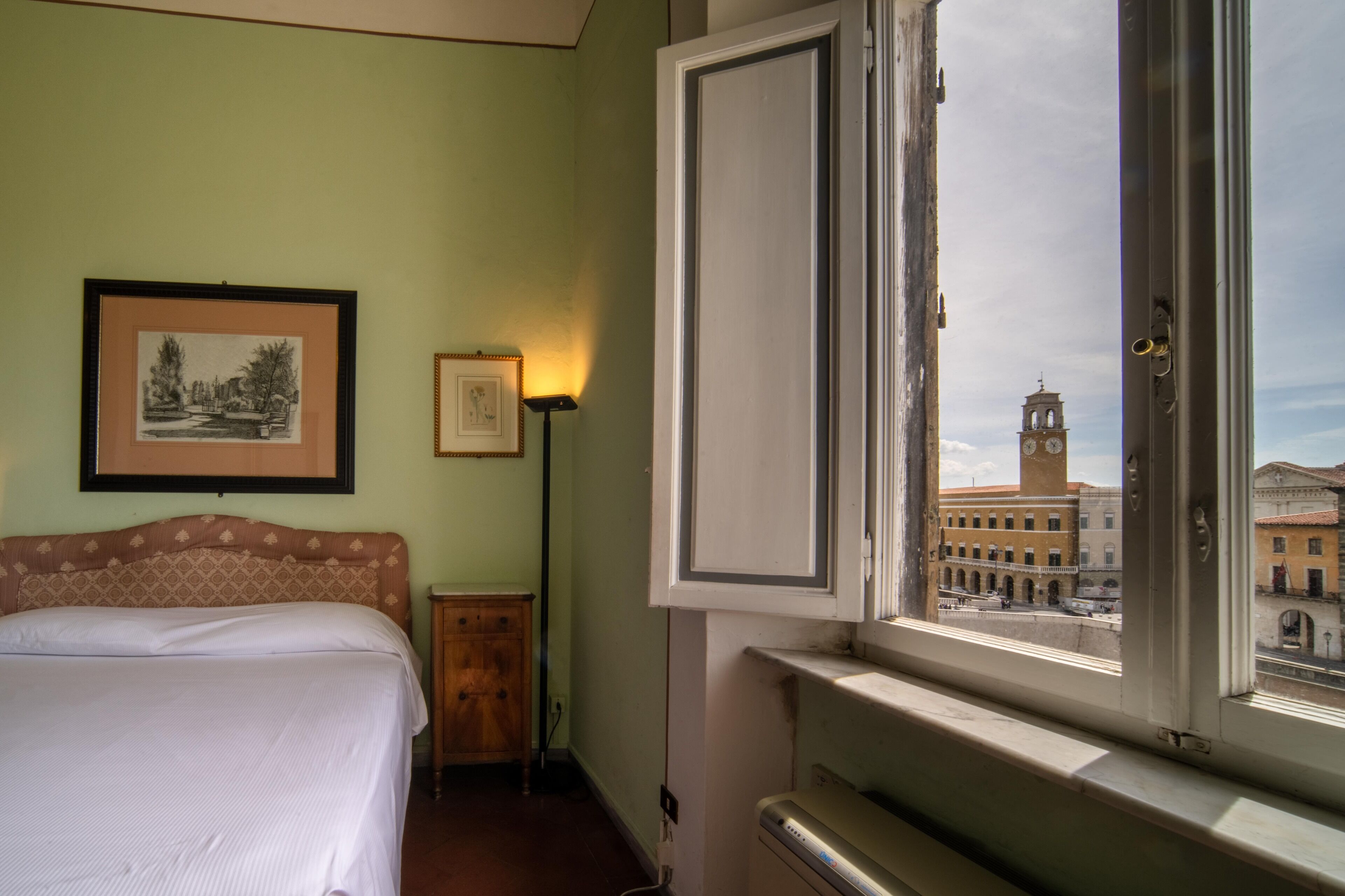 A hotel room with a bed, a nightstand, a lamp, and a window with a view of a clock tower.