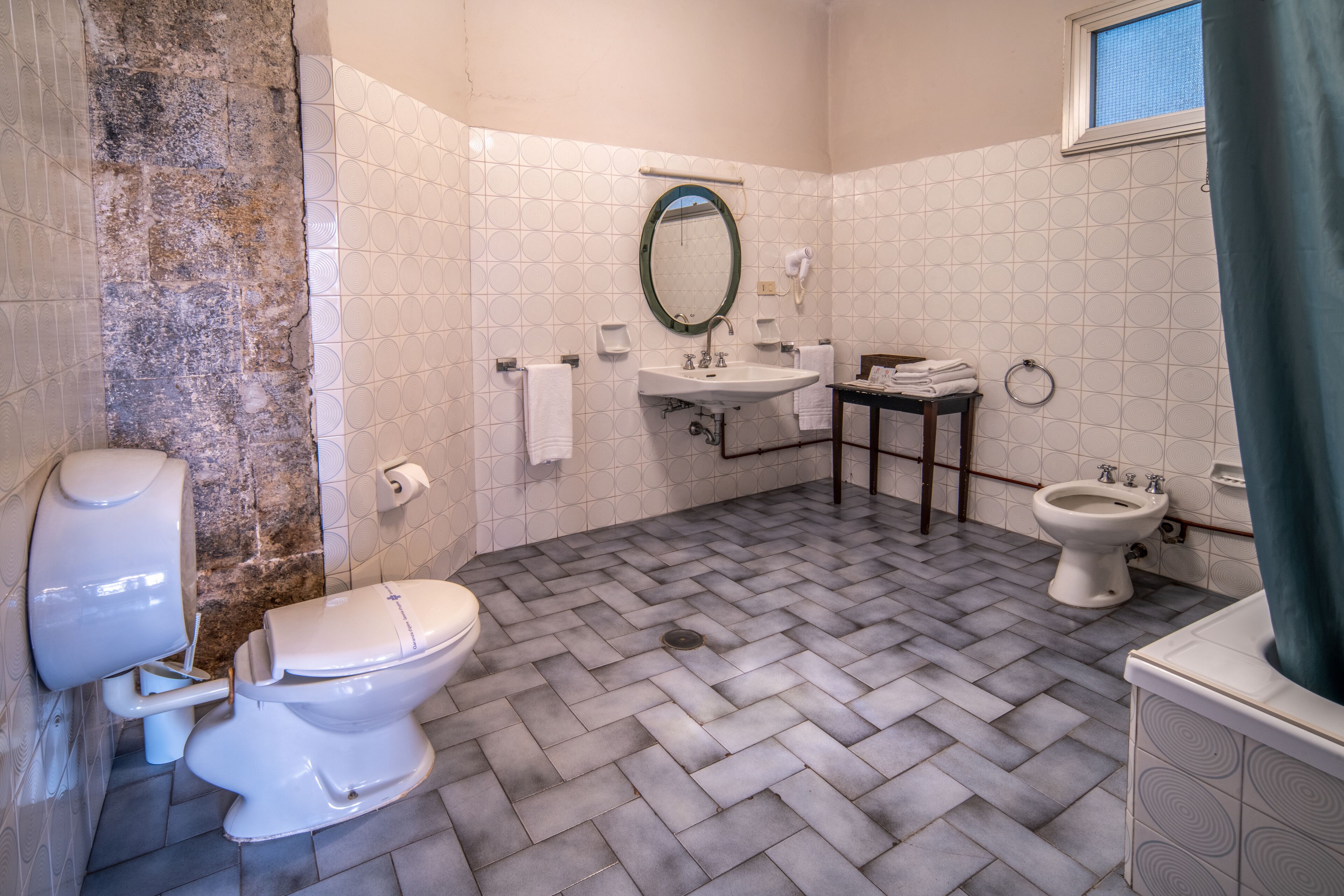 Une salle de bain avec un sol à motifs en chevrons, des toilettes, un bidet, un lavabo et un miroir.