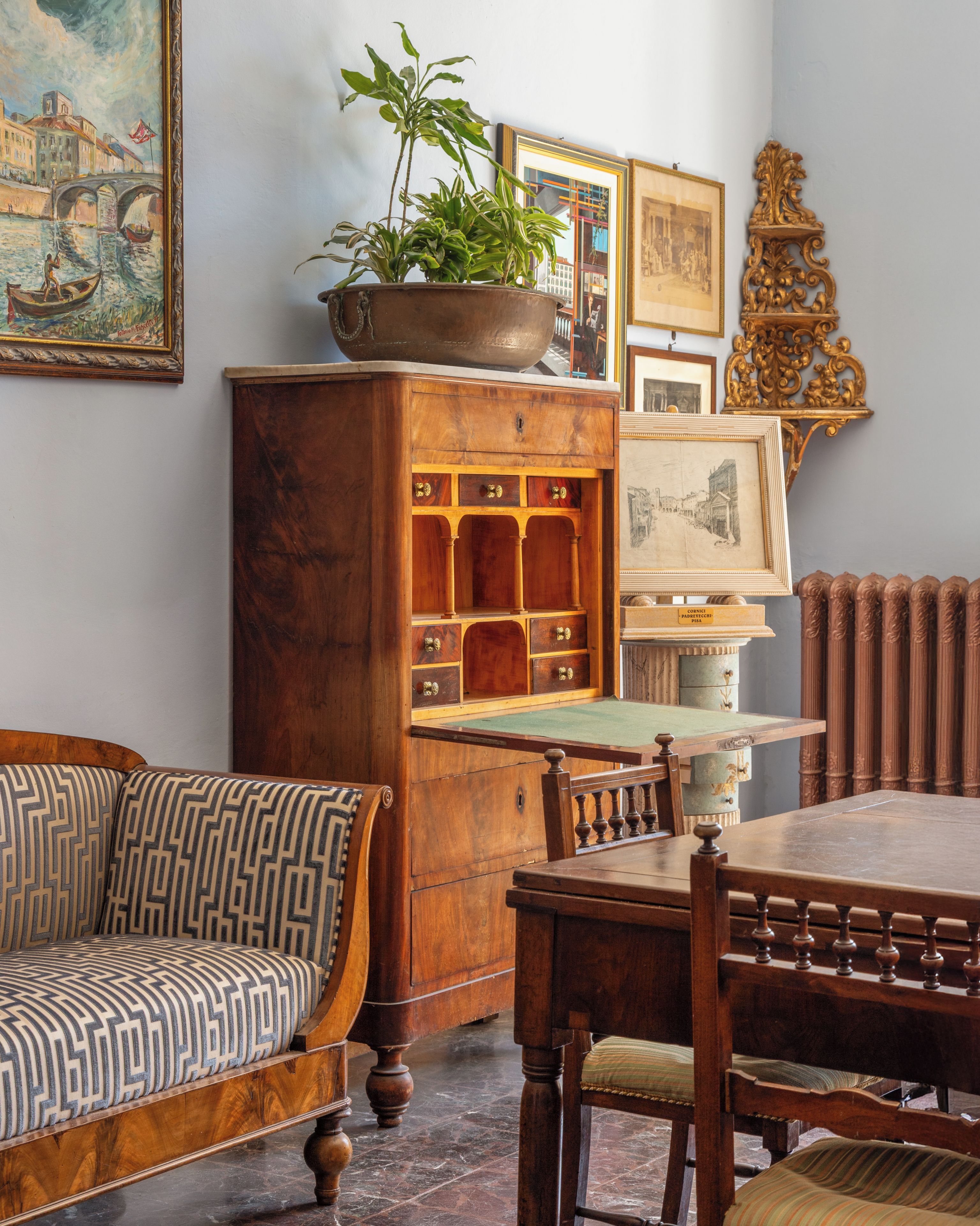 A traditional room with a wooden cabinet, a patterned sofa, a dining table, and various framed pictures on the walls.