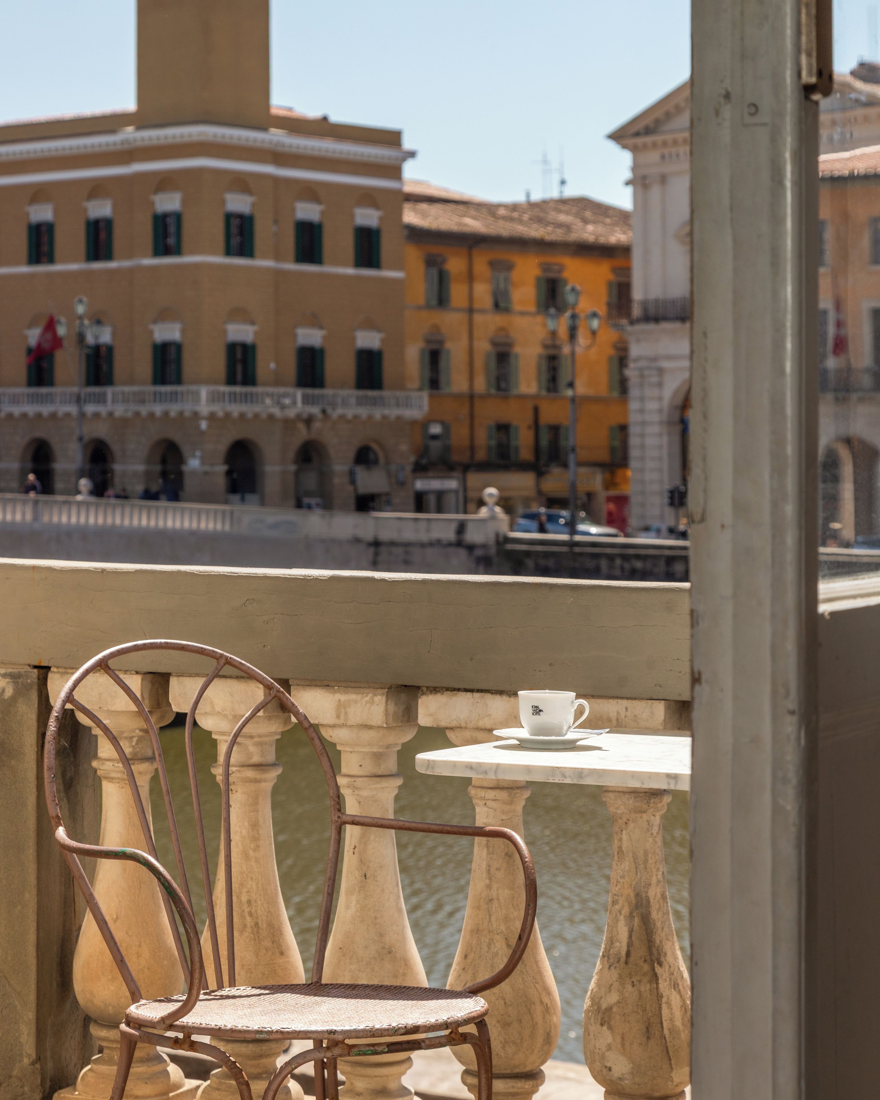 Un balcone con un tavolo e una sedia, affacciato su un canale con edifici sullo sfondo.
