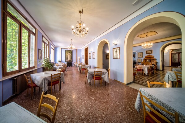 A dining area with multiple tables and chairs, chandeliers, and framed pictures on the walls.