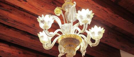 A chandelier with multiple glass flowers and a central glass piece, set against a wooden ceiling.