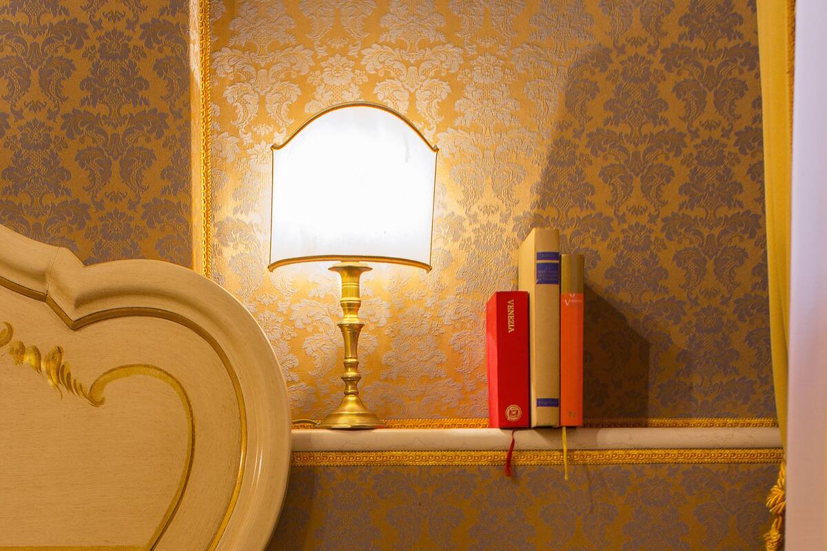 A hotel room with a bed, a bedside table with a lamp, books, and toiletries.