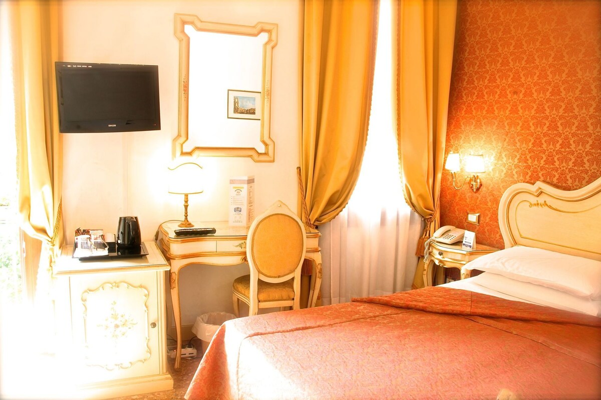 A hotel room with a bed, desk, chair, television, and a telephone.