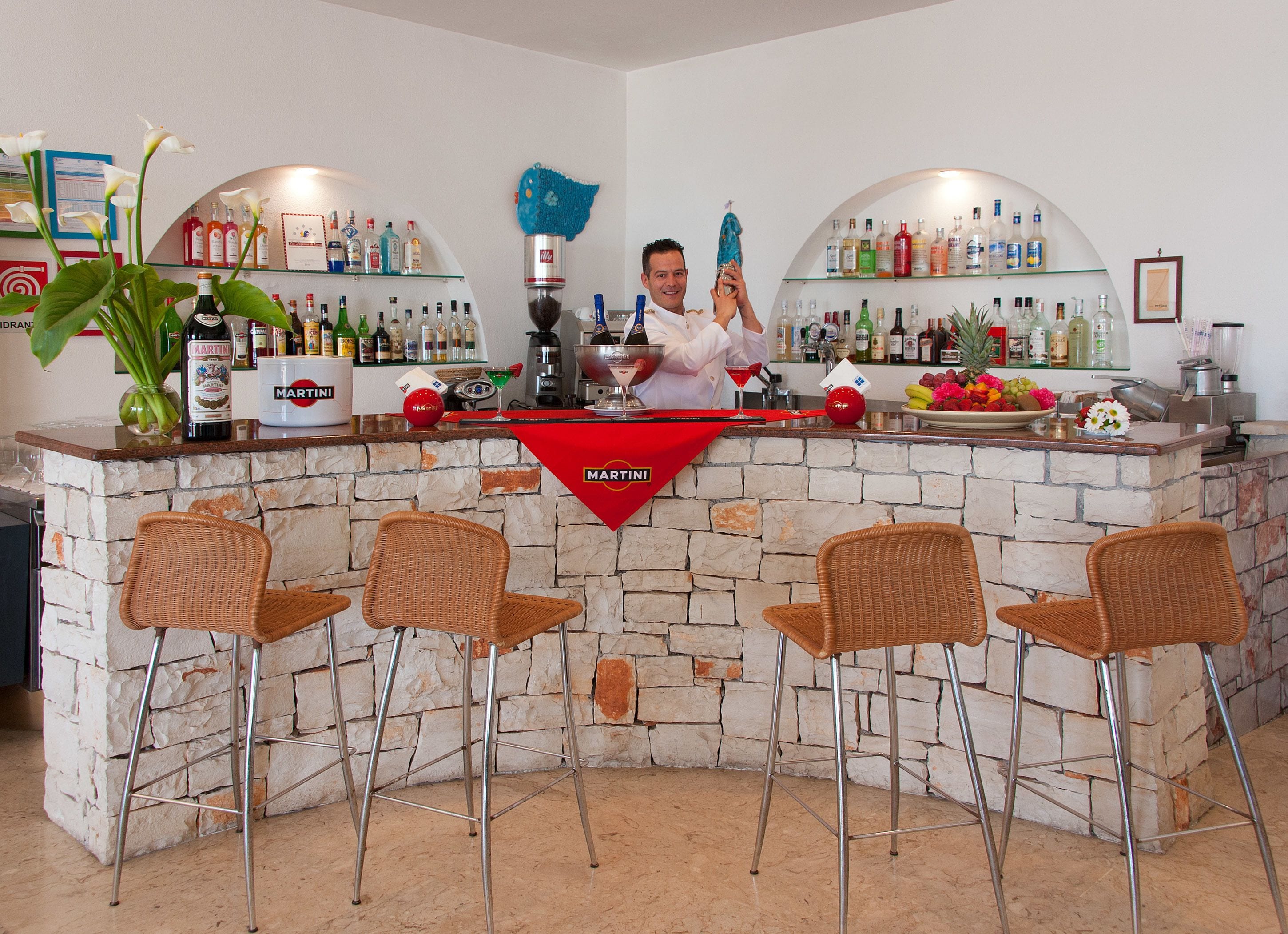 A bar area with a stone wall, wicker chairs, and a variety of liquor bottles.