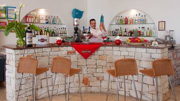 A bar area with a stone wall, wicker chairs, and a variety of liquor bottles.