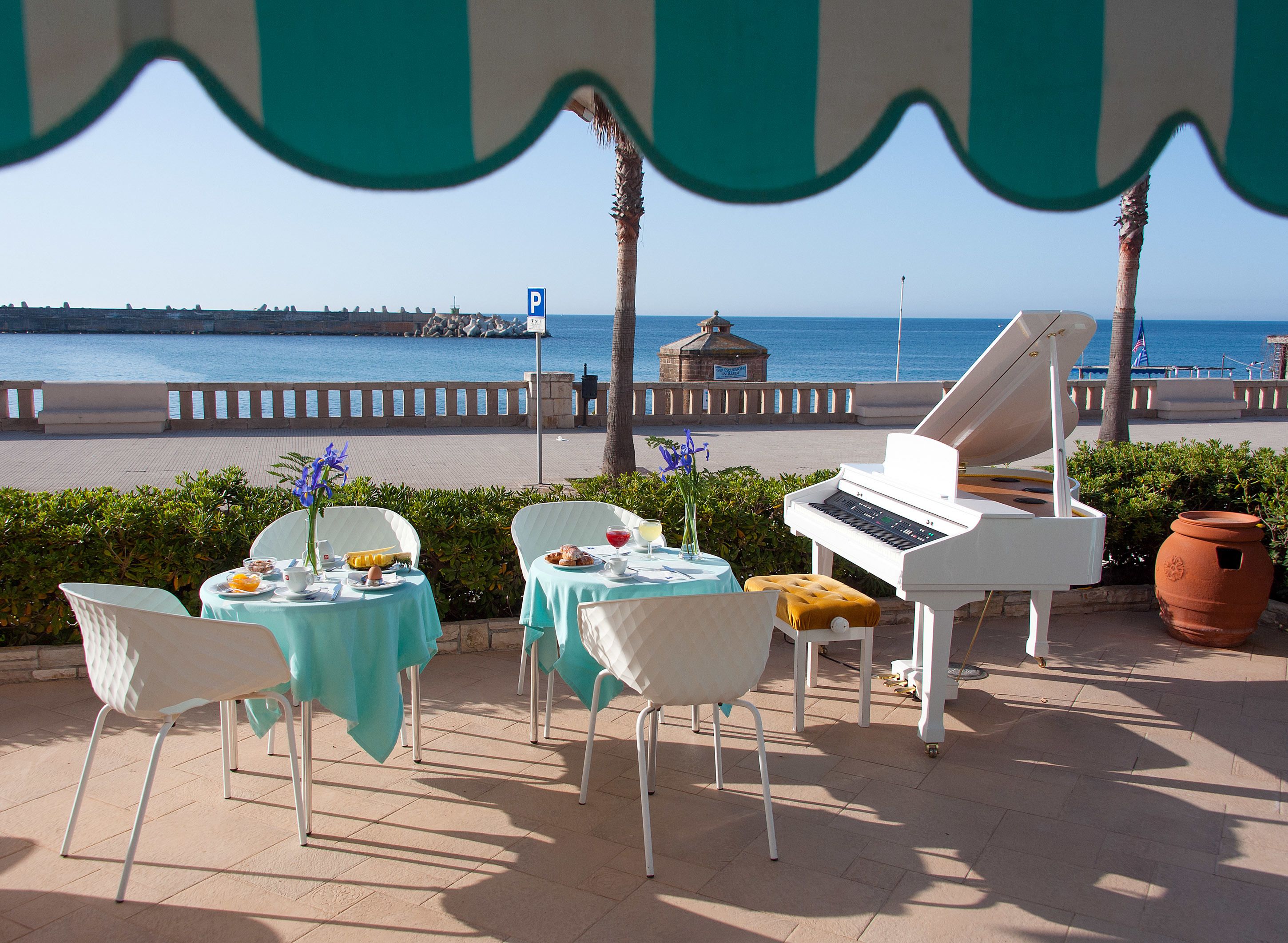 Un área de estar al aire libre con mesas y sillas, un piano de cola y vista al mar.