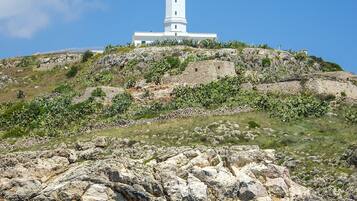Un faro blanco sobre una colina rocosa bajo un cielo azul despejado.