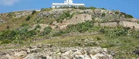 A white lighthouse on a rocky hill with clear blue sky.