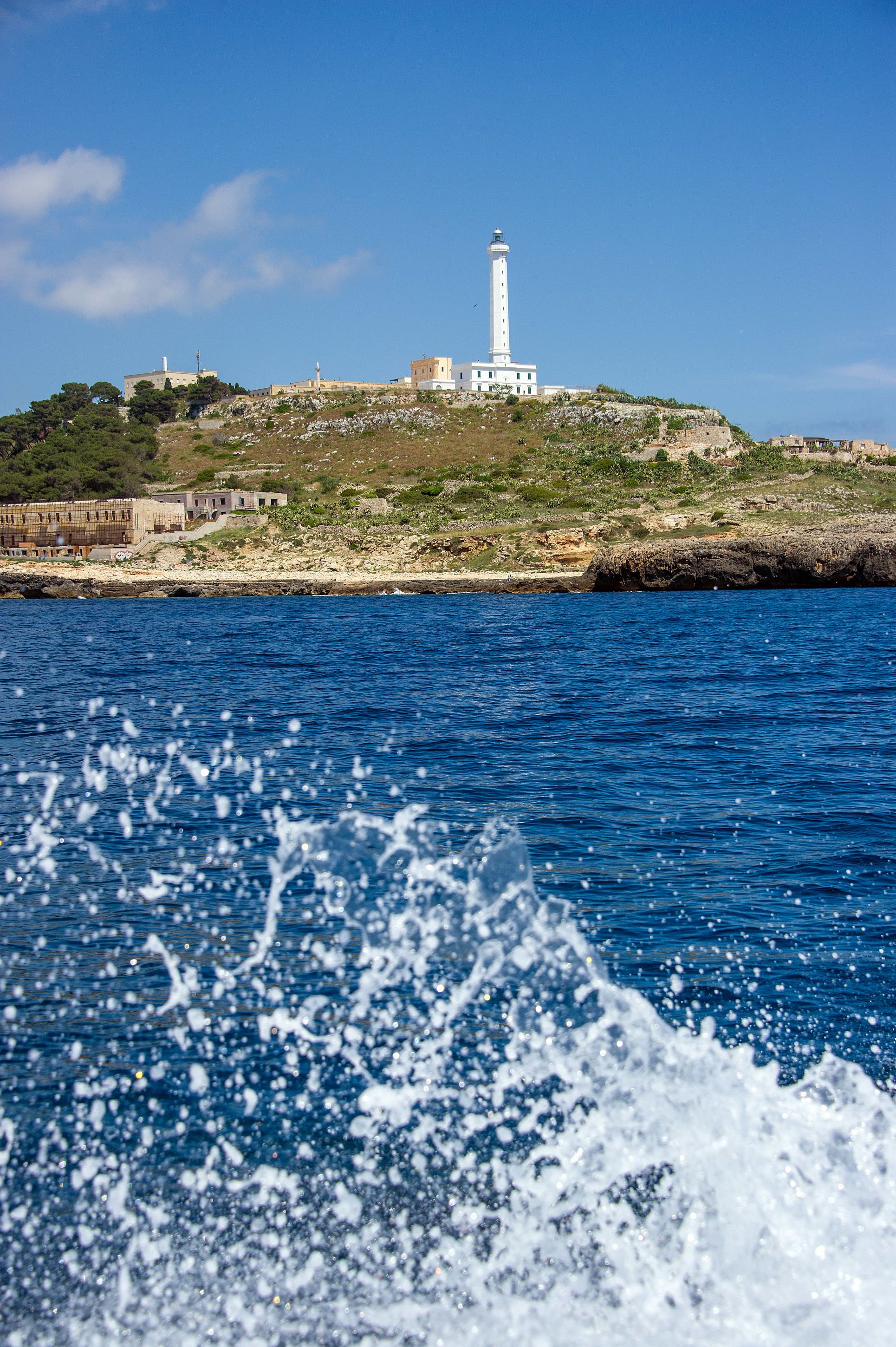 A coastal view with a lighthouse on a hill, a body of water in the foreground, and a rocky shoreline.