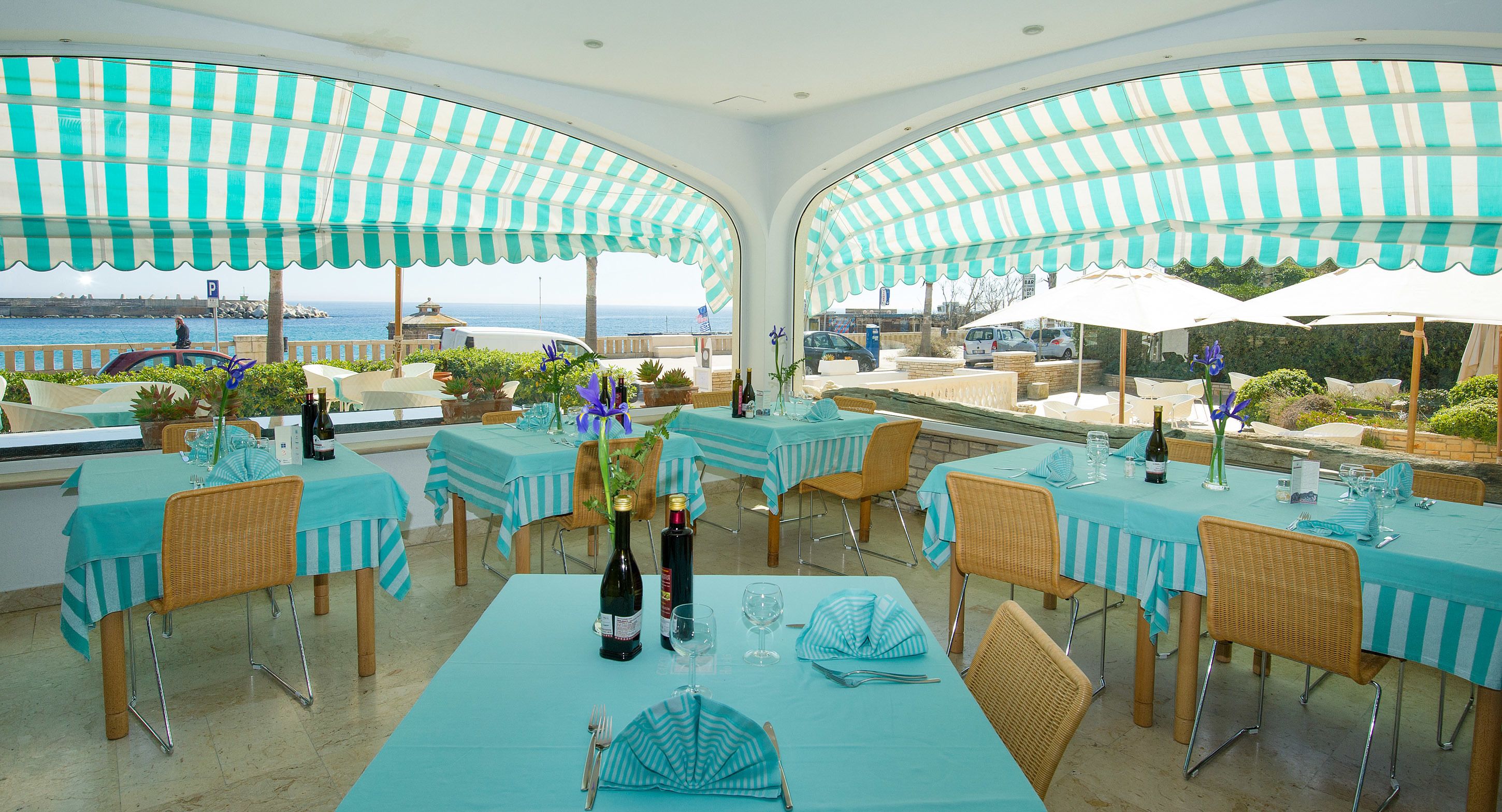 An outdoor dining area with tables and chairs, covered by striped awnings, overlooking a scenic view.