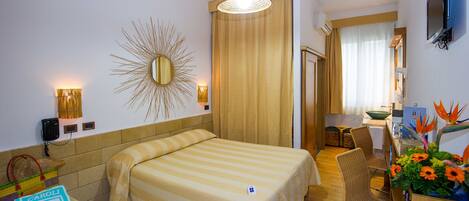 Ein Hotelzimmer mit einem großen Bett, einem Schreibtisch mit Stuhl, einem Spiegel und einem an der Wand montierten Fernseher.