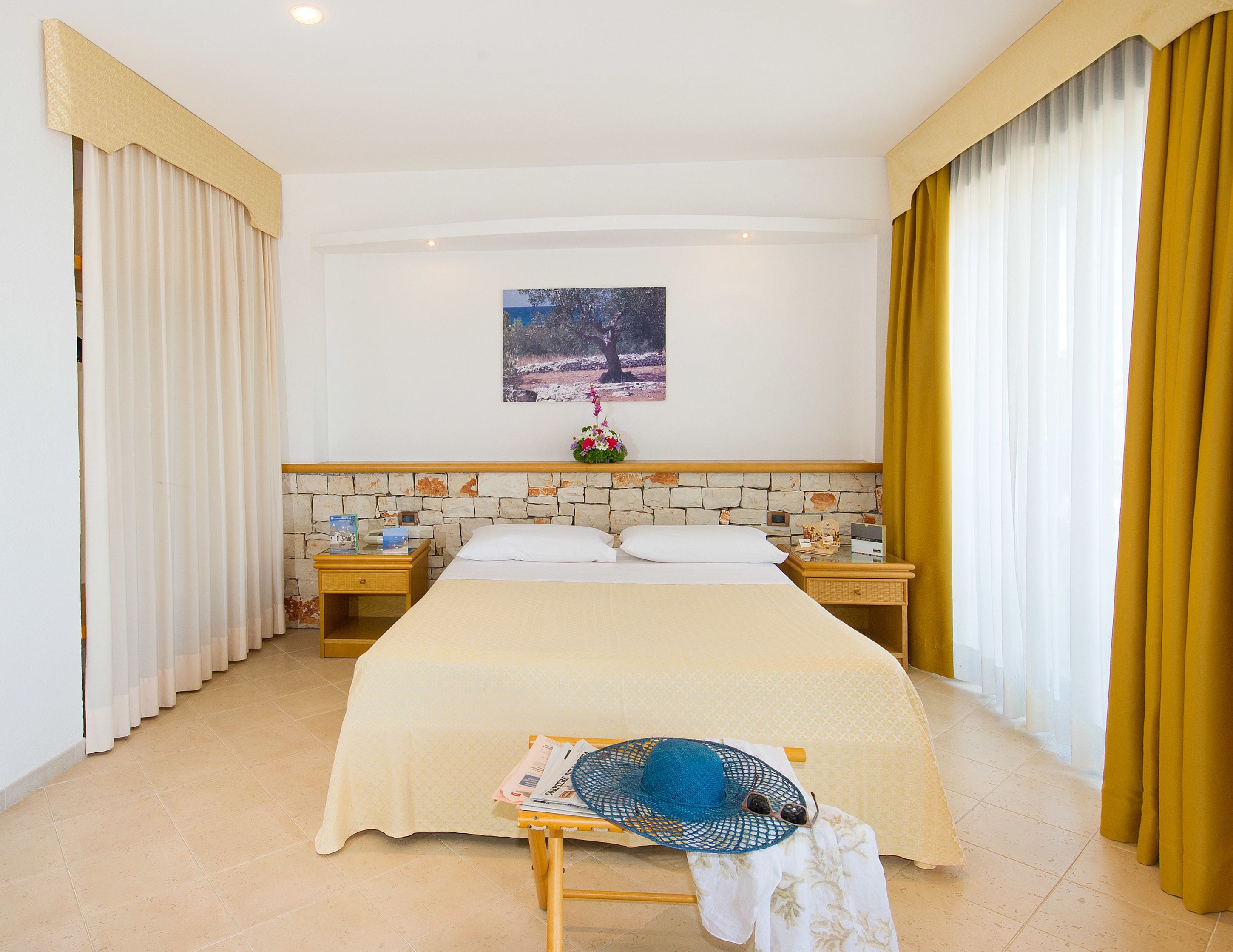 A hotel room with a bed, a nightstand, a wall-mounted painting, and curtains.