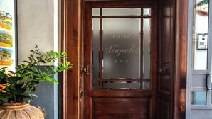A hotel entrance with a wooden door, a doormat with the hotel name, and a potted plant. - Hotel Neapolis (Naples)