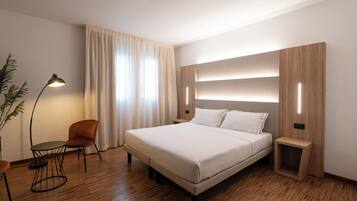 Una habitación de hotel moderna con una cama grande, una mesita de noche, una silla y una lámpara de pie.