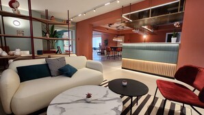 A modern living room with a white sofa, a round marble coffee table, and a red chair. There is a kitchen area with a blue countertop and a hanging light fixture. - Bleis Hotel (Bologna)