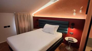 A modern hotel room with a large bed, a small bedside table, and a ceiling light fixture.