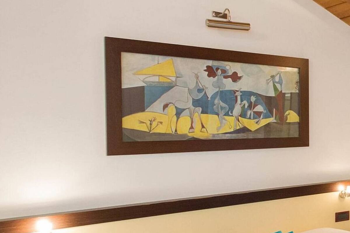 A hotel room with a bed, a nightstand, a wall-mounted light, and a framed abstract painting.