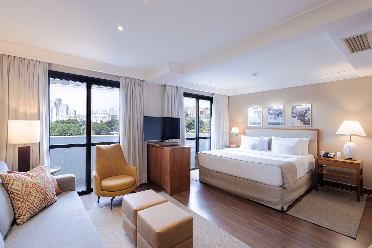A hotel room with a large bed, a TV, a sofa, and a chair.