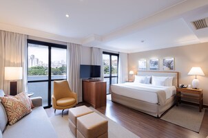 A hotel room with a large bed, a TV, a sofa, and a chair.