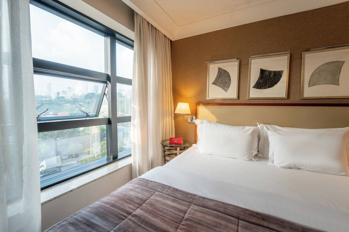 A hotel room with a large bed, a nightstand with a lamp, and three framed pictures on the wall.