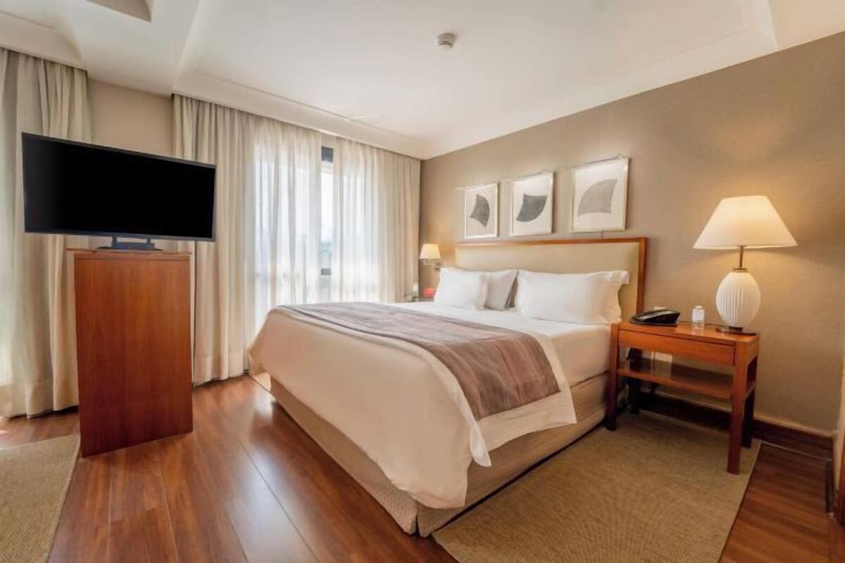 A hotel room with a large bed, a TV, a wooden nightstand, and a desk lamp.