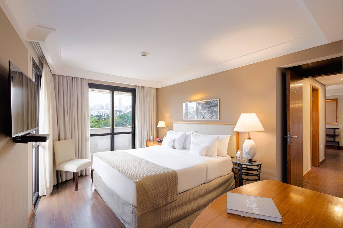 A hotel room with a large bed, a desk, a chair, a TV, and a window with curtains.