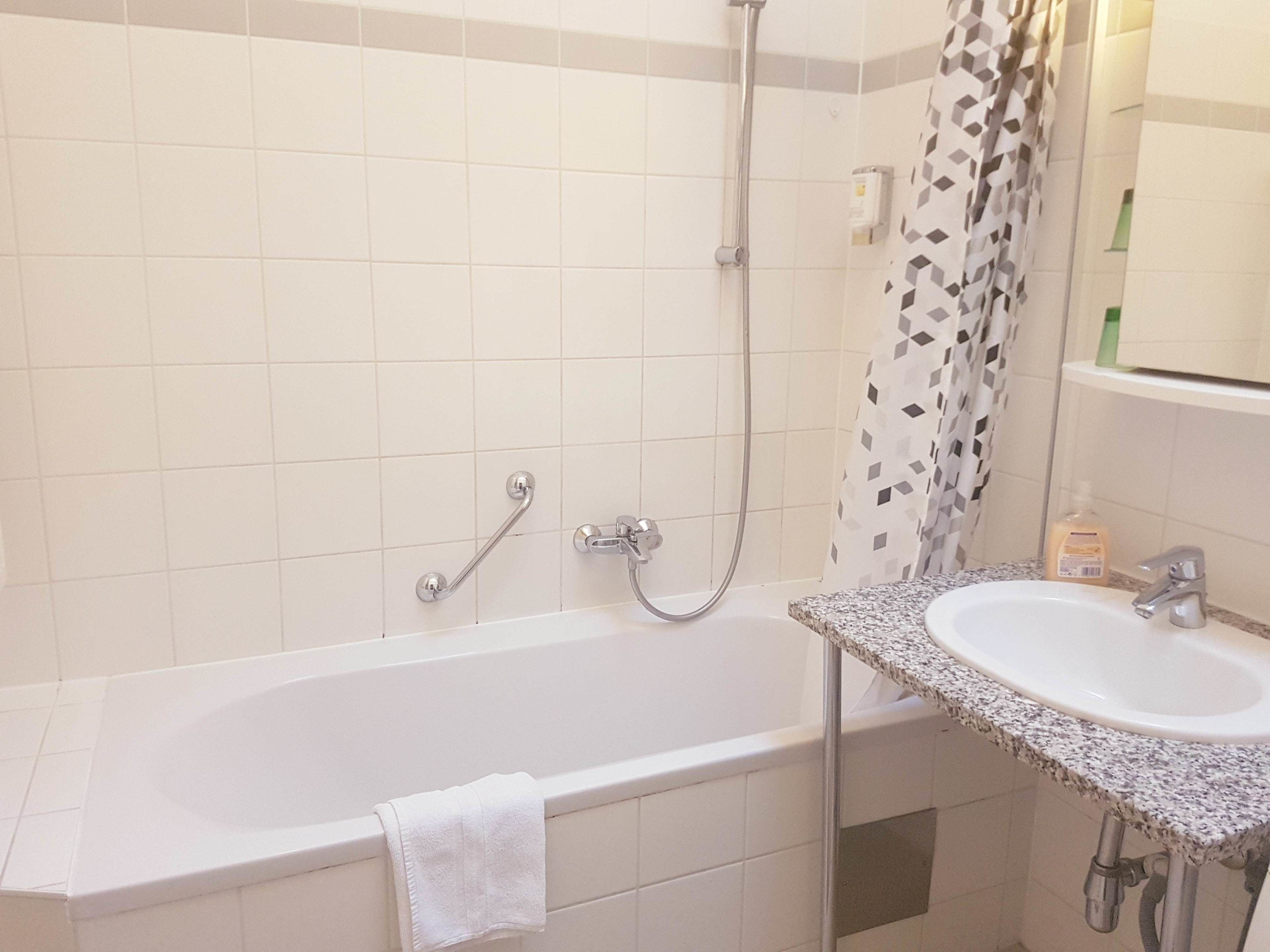 Un baño con una bañera blanca, ducha, lavabo con encimera de granito y una toalla colgada en la bañera.