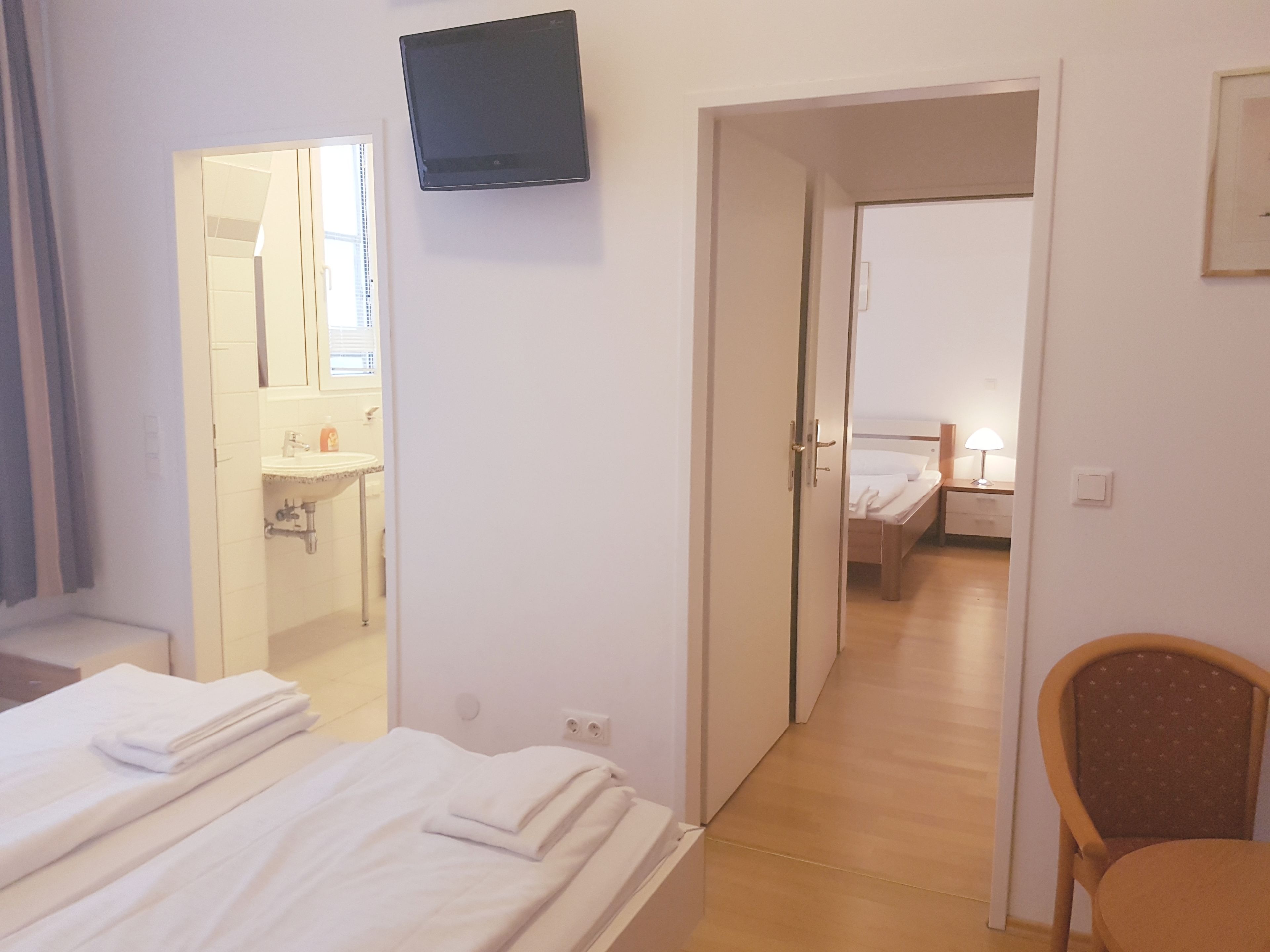 A hotel room with a bed, a TV mounted on the wall, a bathroom with a sink and mirror, and a chair.